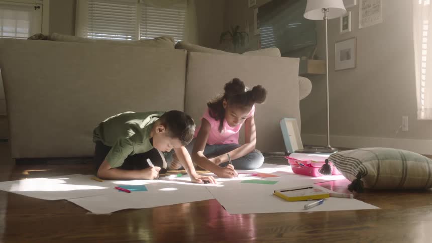 Children sitting on the floor drawing on cardboard in the living room