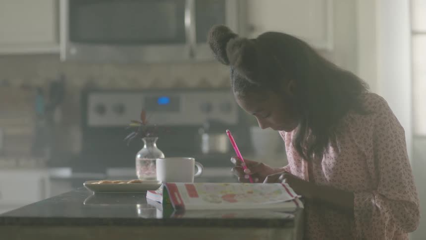A black female in the kitchen sitting on the dinning while doing her homework