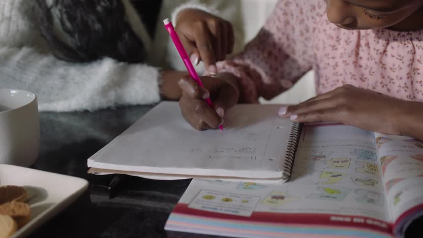 Mother assisting her daughter who is writing in a notebook