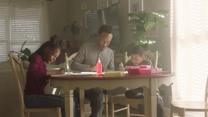 Father helps his son and daughter with homework at home