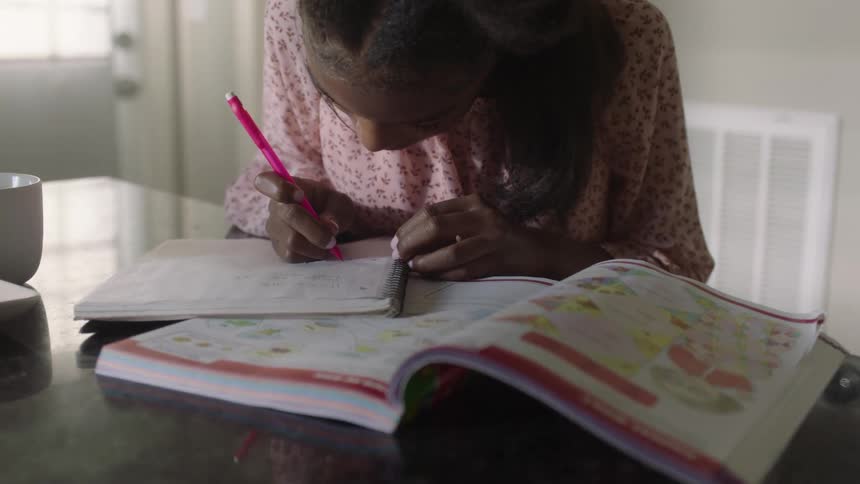 A little girl is writing on paper using a red pen