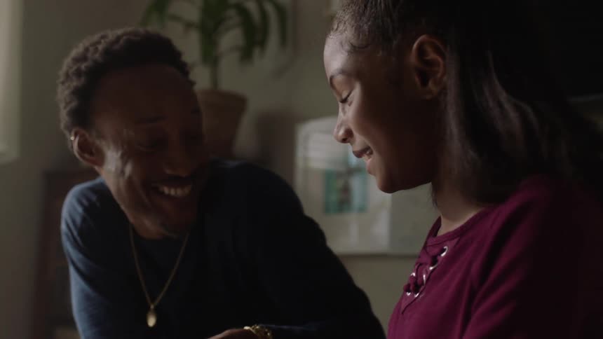 An adult and a child girl are playing with a toy on the glass table and they are both smiling
