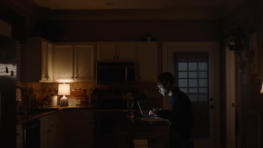 Man sitting in the kitchen typing on the laptop at night