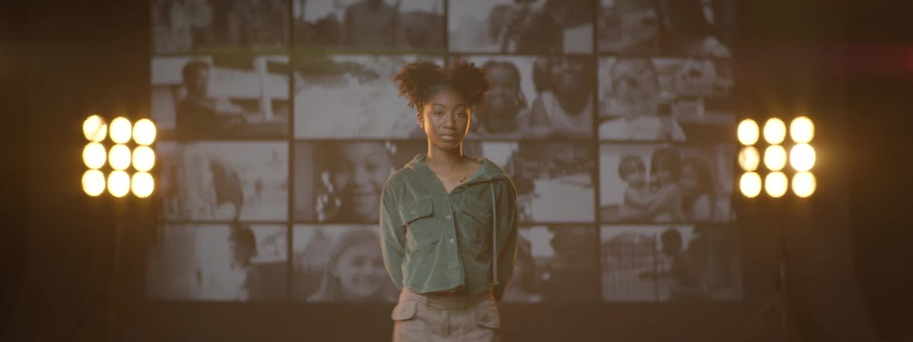 Portrait of a girl with arms crossed in front of a screen playing footage