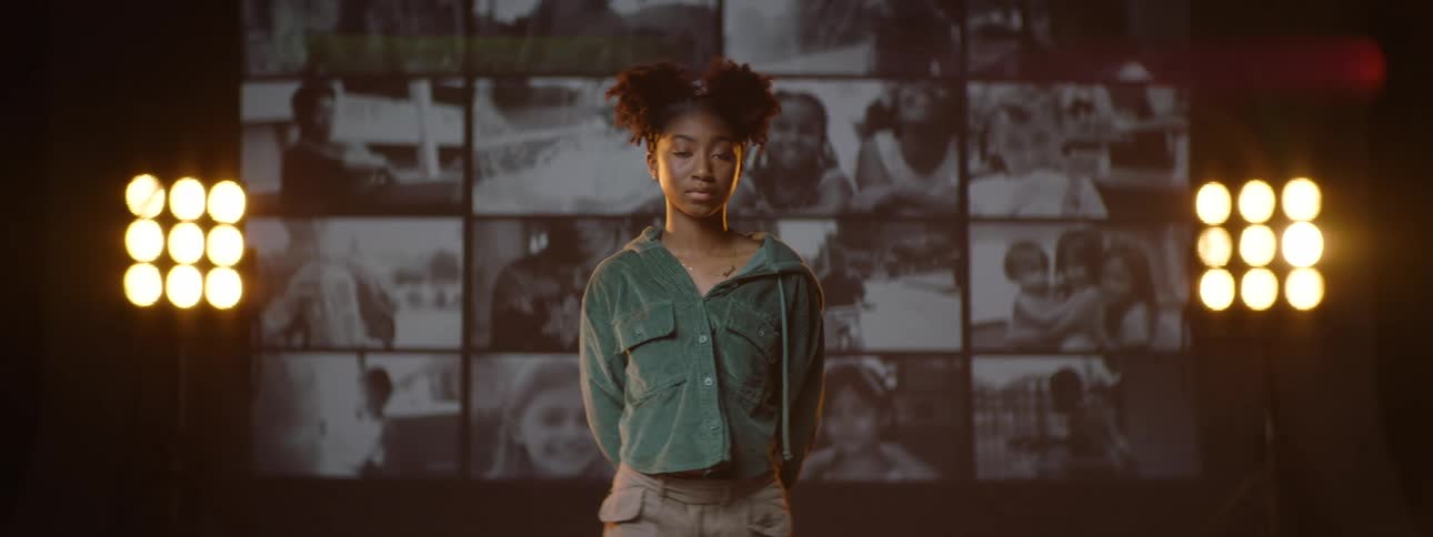 Young girl stands on a stage in front of a wall of screens