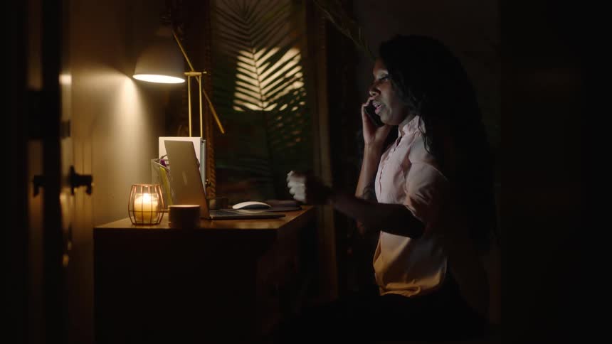Woman sitting and talking on the phone in front of a table with her laptop