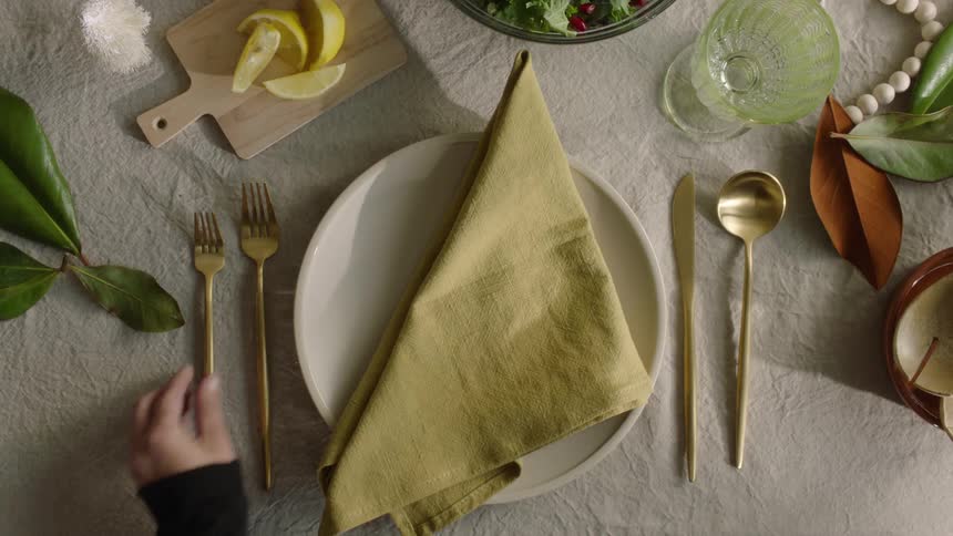 A hand finishes setting a table by carefully putting down a fork