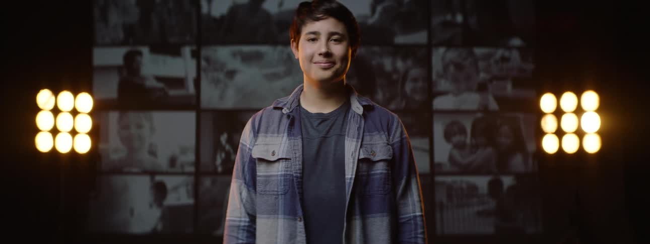 Portrait of a boy giving a smile with a screen showing footage just behind him