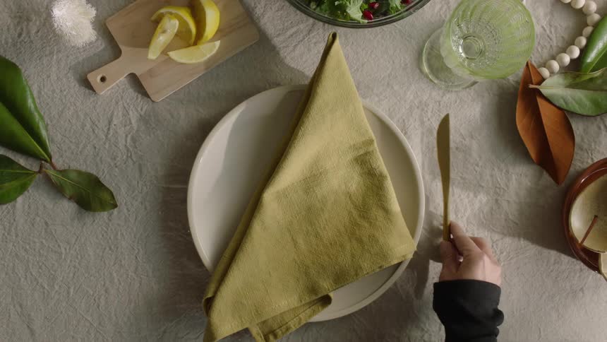 A person setting up a dining table by arranging the plates napkin and cutlery