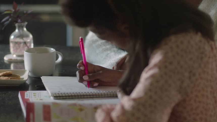 Mother sitting next to her daughter who is writing