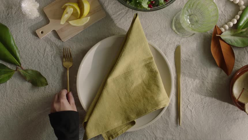 A human hand placing a golden fork on a table with a plate and other objects