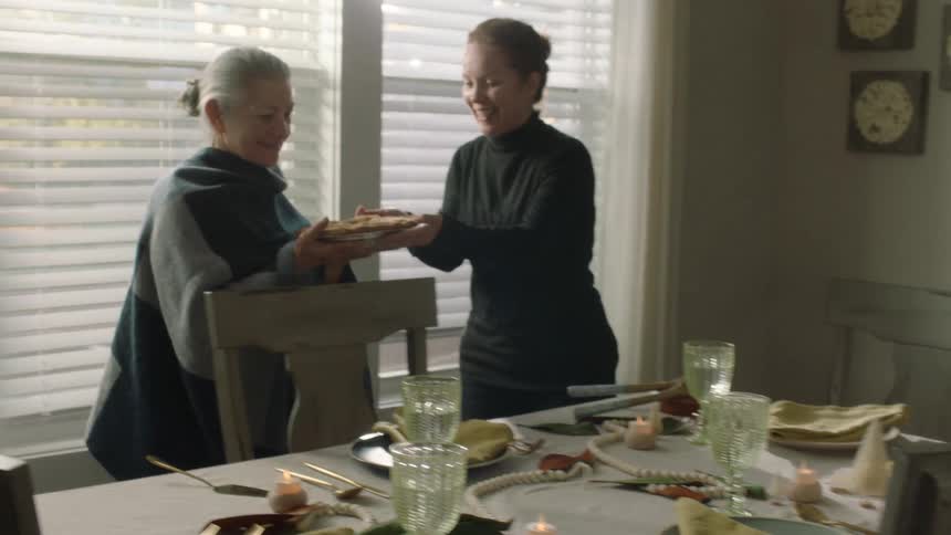 A woman places a pie on the dining room table