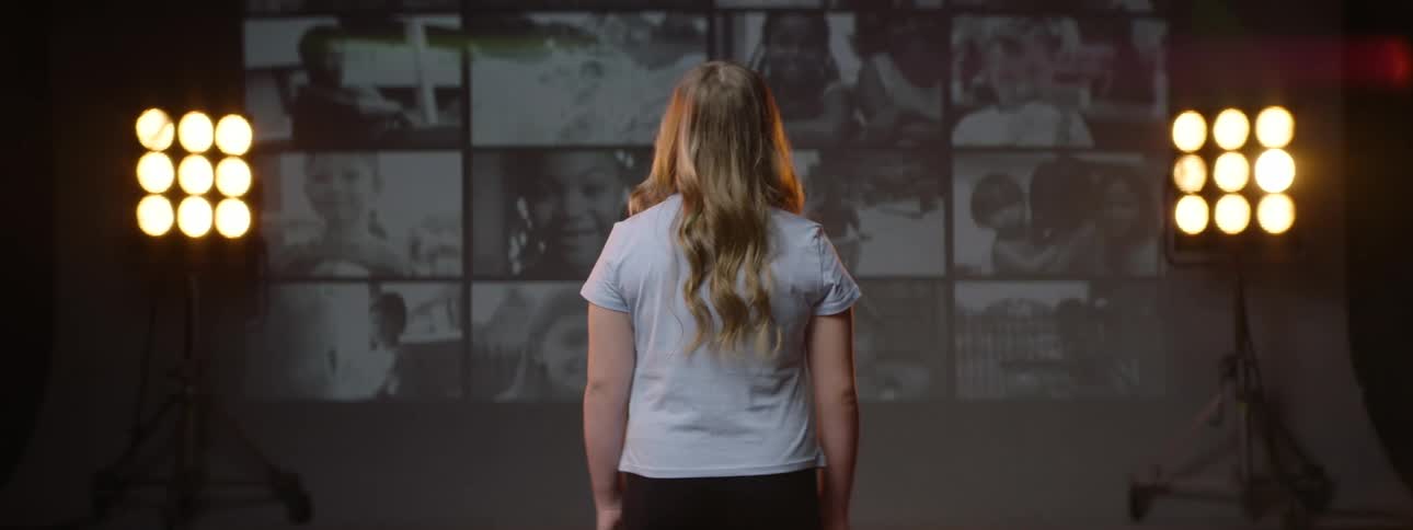 Back of a blonde woman looking at a wall with multiple screenstion