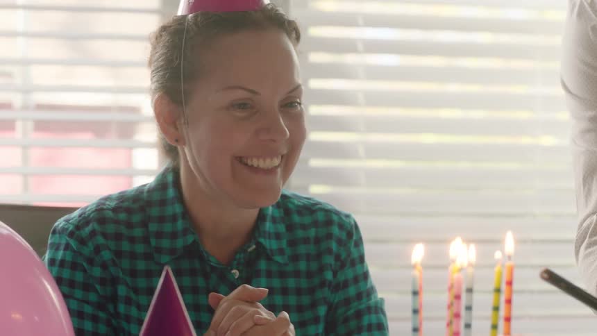 Woman claps and smiles in front of a birthday cake