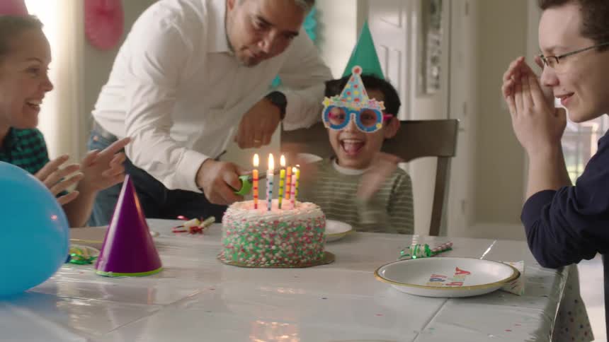 Young boy smiling and clapping while the father light the candles on the birthday cake
