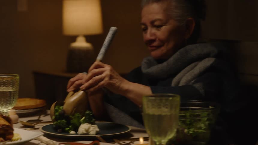 Elderly woman putting vegetables on her plate at a dinner table in the evening