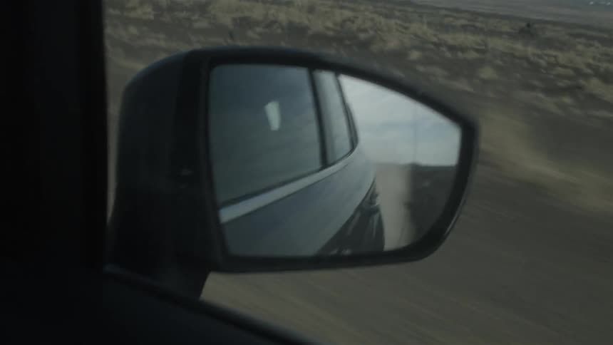 Dirt is flying behind a vehicle in the rear view mirror