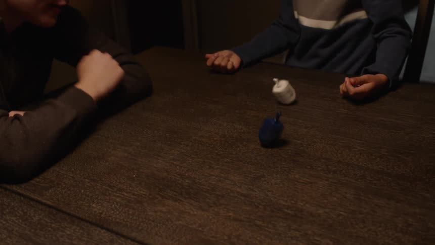 Two boys playing with dreidels on a dinner table