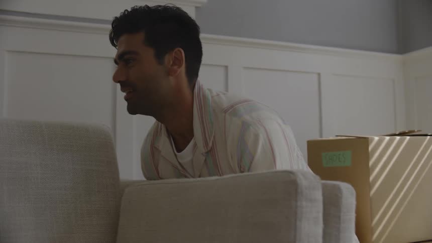 Man and woman placing a sofa in the corner of the house then sitting down and conversing with each other