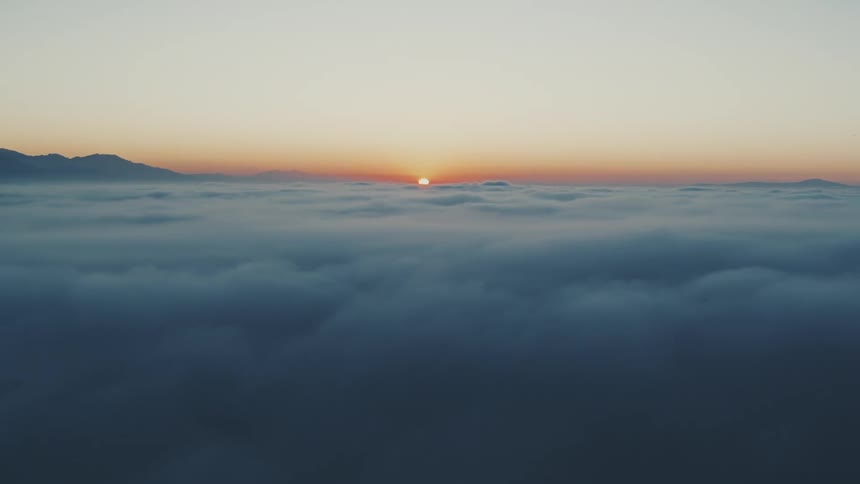 The sun rises in the distance over a vast landscape of clouds at dawn