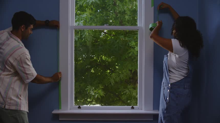 Young couple taping a windowsill for painting