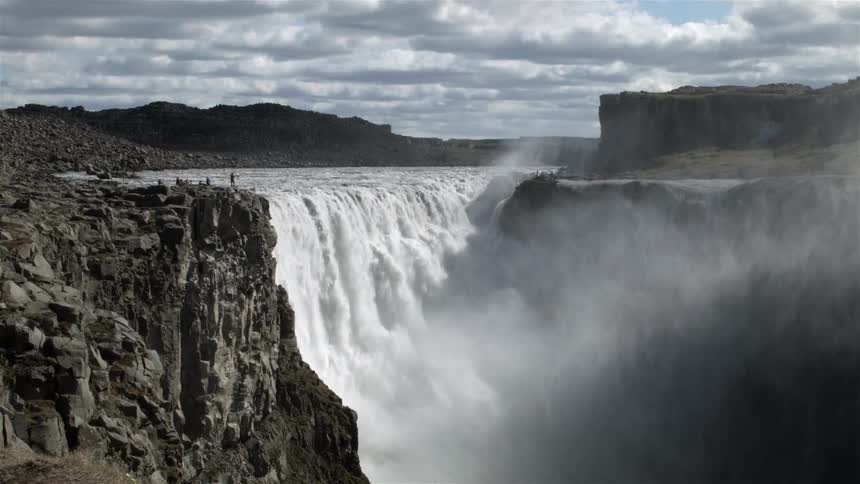 People are on the edge of a cliff watching a waterfall