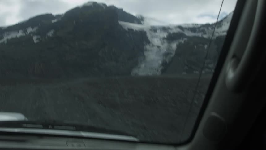 Mountain covered with some snow as seen through a moving windshield