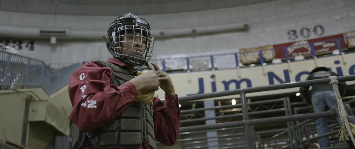 A man is latching his helmet on in a bull ring