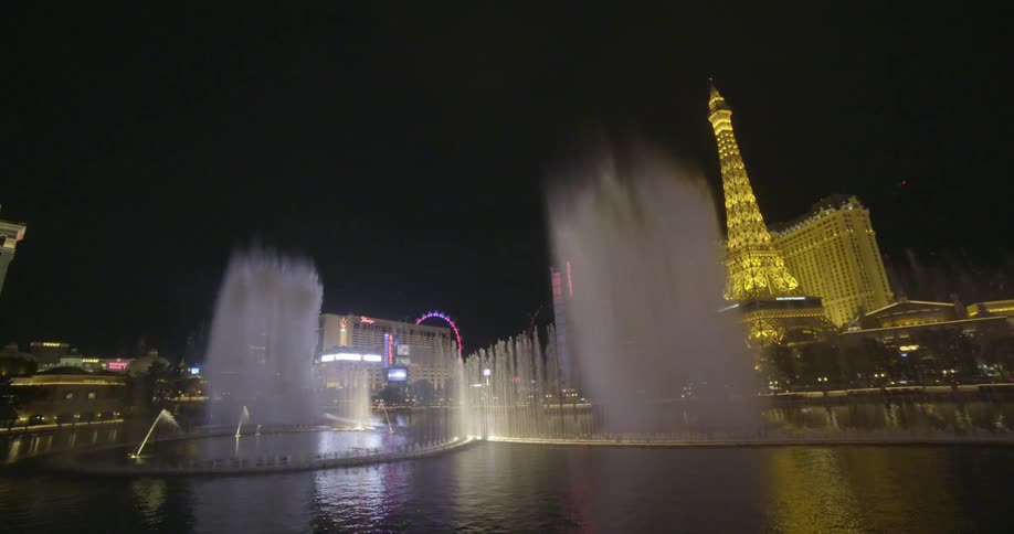 A fountain pours into the air in front of casinos at night