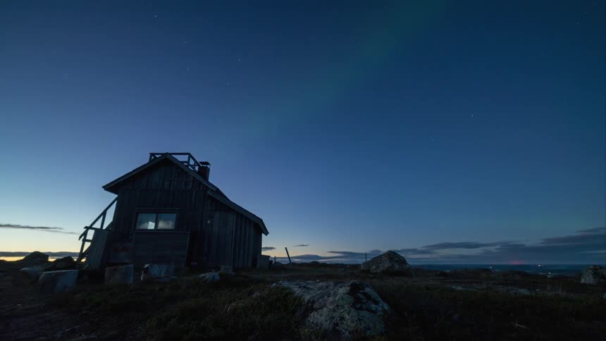 Day to night time-lapse with green auroras behind a remote cabin