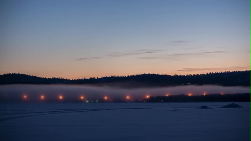 Fog traveling across snowy field at sunset