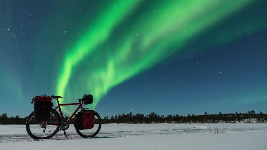 A bike sits on a snow covered field as green flares fill the sky