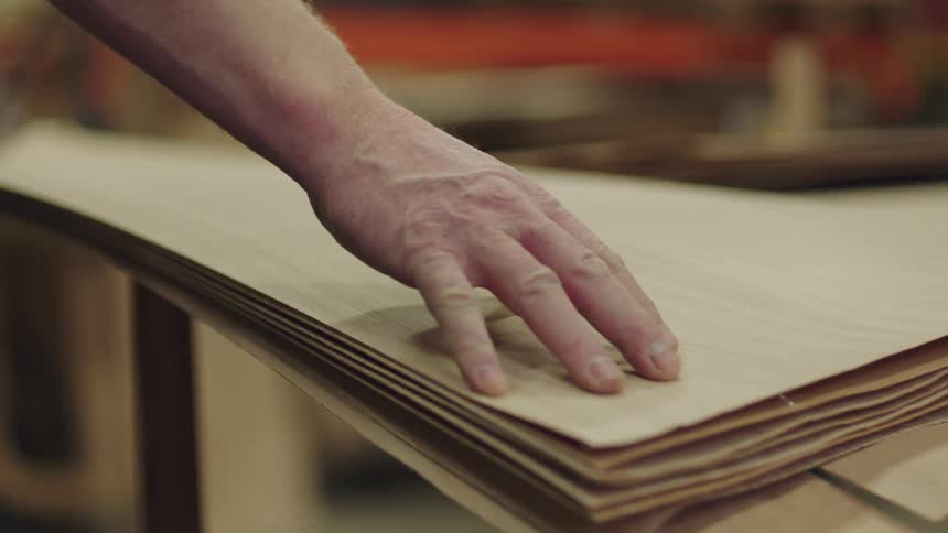 A human hand running its fingers across the surface of a thin piece of wood