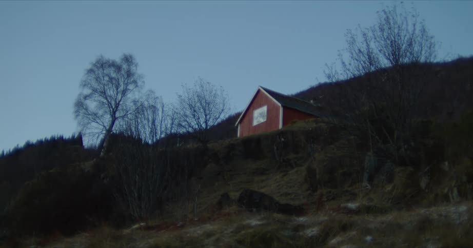 A small red house sits alone on a hillside on a clear winter day