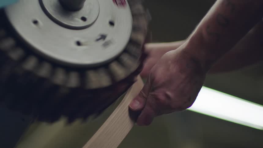 A person holding wood passing through a polishing machine
