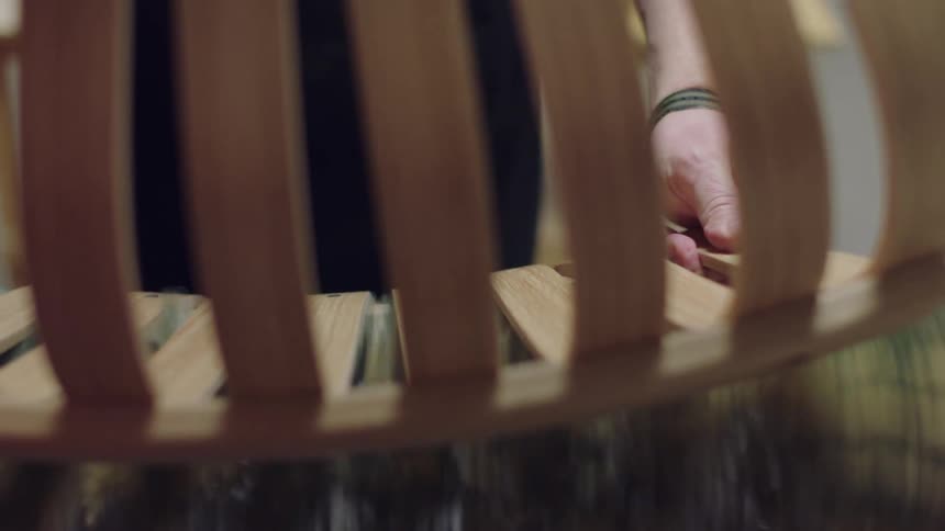 A mans hands passing wood on a rotating sandpaper