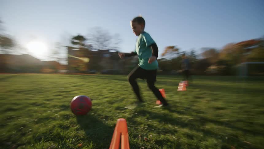 A child kicks the soccer ball around the cones