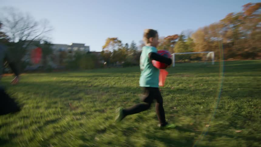 Children run on the soccer field carrying balls