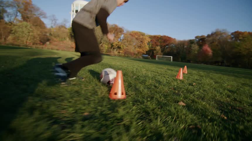 Boy practicing with a soccer ball weaving through cones on the grass field