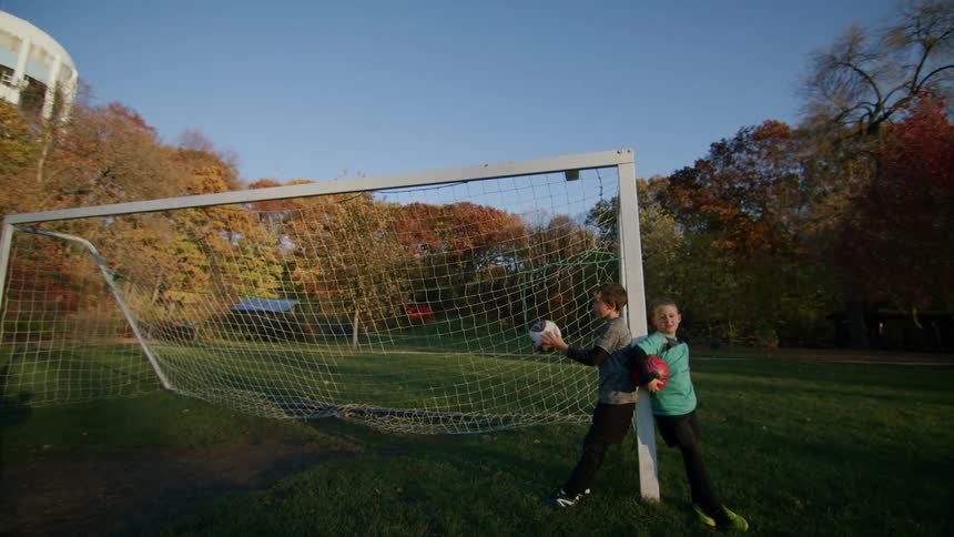 Two boys leaning against the goal post with balls in their hands