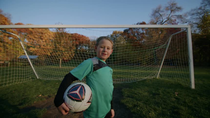 Boy posing in front of a goal on a field holding a soccer ball