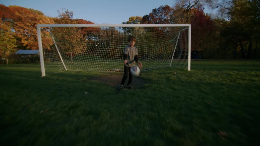A kid playing soccer and running away from a goal post