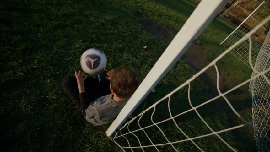 A boy sitting on the grass throwing a ball into the air