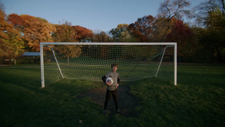A child is standing in front of the net holding a soccer ball