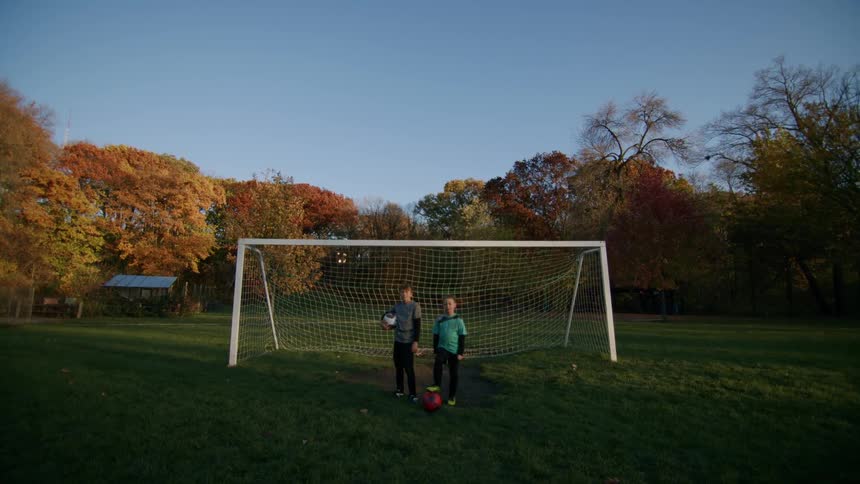 Two boys with their backs to the sun posing with soccer balls