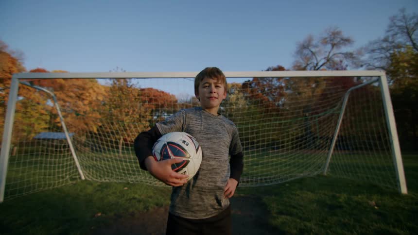 Boy with his back to a goal on a soccer field posing while holding a ball