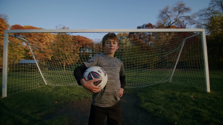 Young boy holds a soccer ball while standing at the goal post during the day