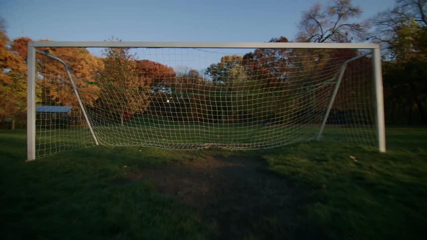 Two boys playing soccer as the run with separate the balls away from the goal post