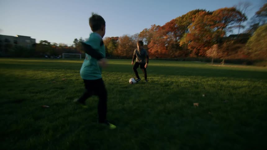 Two boys play soccer in a grass covered field
