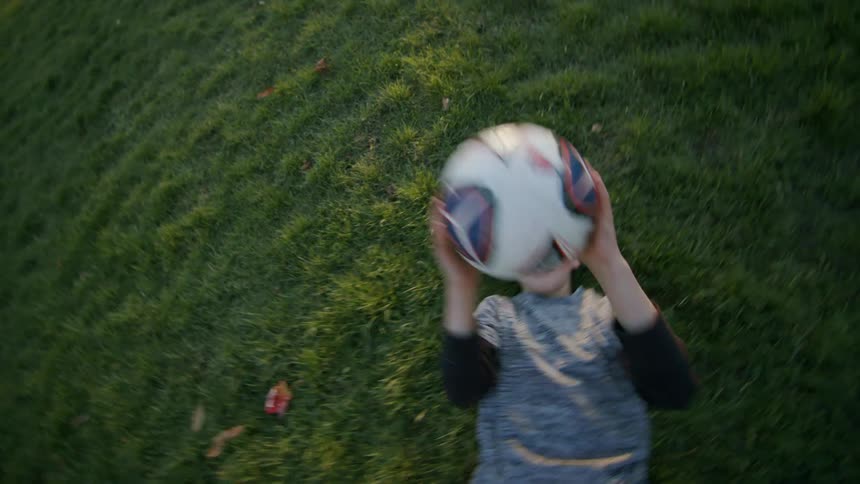 Boy lying on the grass plays with a soccer ball on the soccer field